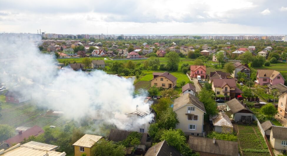 Aerial view of a house on fire with orange flames and white thick smoke