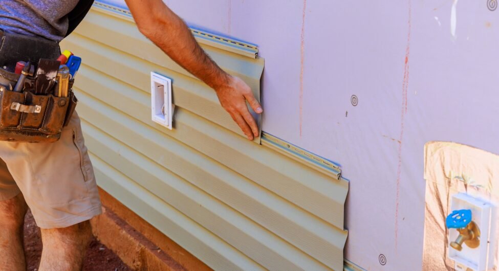 An employee installs vinyl plastic siding panels on wall facade of a new residence