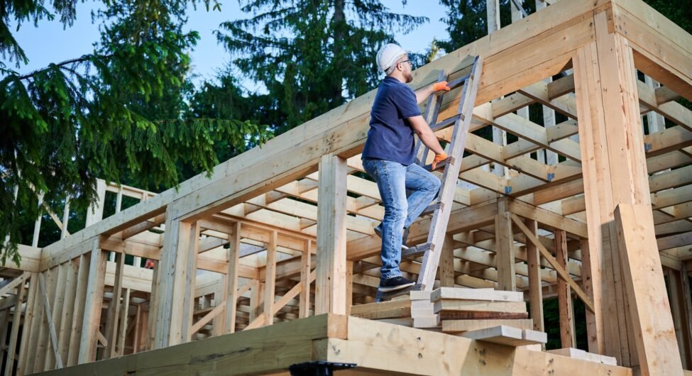 Bearded man with glasses climbing ladder to the second floor of the two-story building.