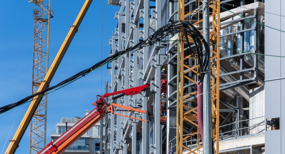 A construction site with cranes and workers on a high-rise building against a clear blue sky