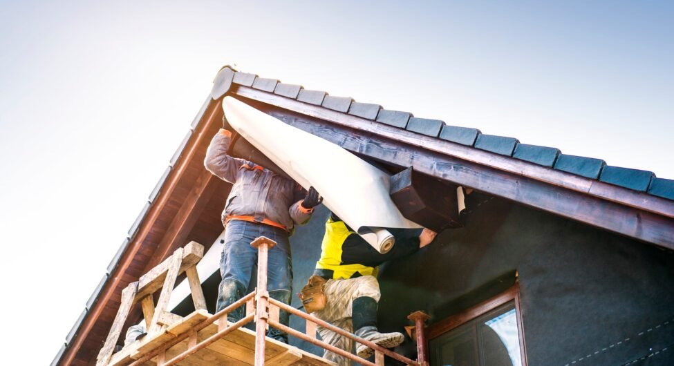 Construction workers thermally insulating house with glass wool and foil.