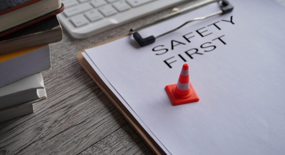 Miniature safety cone on top of paper clipboard with text SAFETY FIRST.